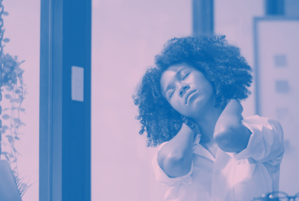 Image of woman at desk holding back of neck with eyes closed. Purple decorative tint to photo.